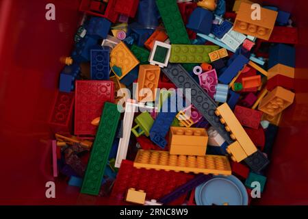 Una collezione di giocattoli lego prelevati a caso su un contenitore rosso. Foto Stock