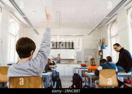 Vista posteriore dello studente che solleva la mano mentre frequenta una lezione in aula Foto Stock