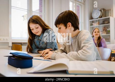 Ragazzo che aiuta una donna amica mentre studia insieme seduto alla scrivania in classe Foto Stock