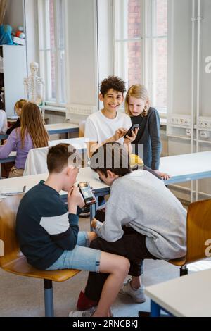 Studenti maschi e femmine che utilizzano smartphone seduti alla scrivania in classe Foto Stock