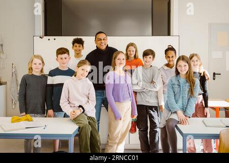 Ritratto di studenti sorridenti e multirazziali in piedi con un insegnante maschio alla scrivania in classe Foto Stock