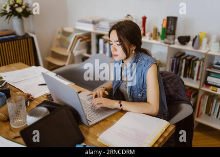 Giovane donna che usa un notebook mentre fa un compito scolastico a casa Foto Stock