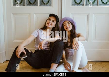 Ritratto di giovani donne felici sedute contro la porta bianca a casa Foto Stock