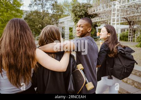 Un giovane sorridente che guarda indietro mentre cammina con gli amici in città Foto Stock
