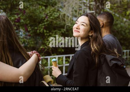 Giovane donna sorridente che tiene un gelato mentre cammina con gli amici Foto Stock