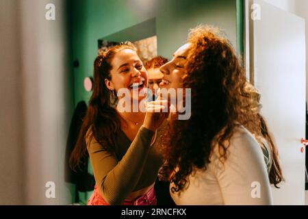 Giovane donna allegra che aiuta un amico con il trucco a casa Foto Stock