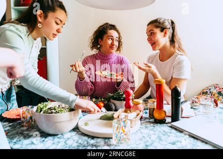 Donna che serve il pranzo mentre le amiche parlano a casa Foto Stock