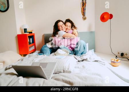 Felici giovani amiche che si abbracciano mentre sono sedute a casa Foto Stock