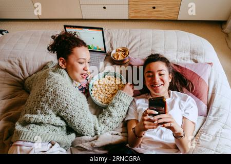 Felici amiche con smartphone e laptop che trascorrono il tempo libero a casa Foto Stock