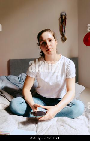 Ritratto di giovane donna seduta a letto a casa Foto Stock
