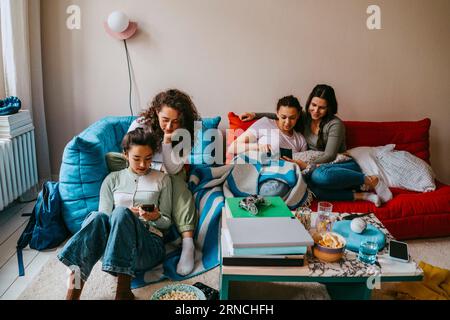 Giovani amiche che usano i telefoni cellulari a casa Foto Stock