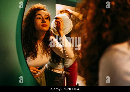 Giovane donna che applica mascara mentre guarda allo specchio Foto Stock