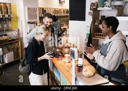 Buon cassiere che parla con i clienti al banco cassa del supermercato Foto Stock