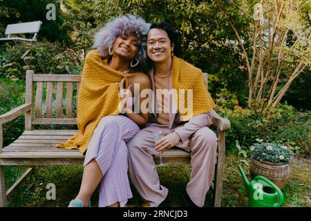 Ritratto di amici LGBTQ sorridenti seduti insieme sulla panchina durante la cena nel cortile posteriore Foto Stock