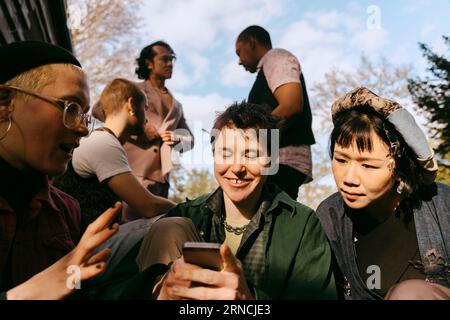 Curiosi amici LGBTQ che condividono uno smartphone durante la cena in giardino Foto Stock