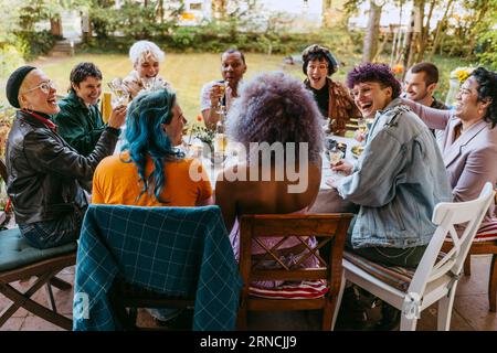 Amici felici della comunità LGBTQ che applaudono durante la cena in cortile Foto Stock