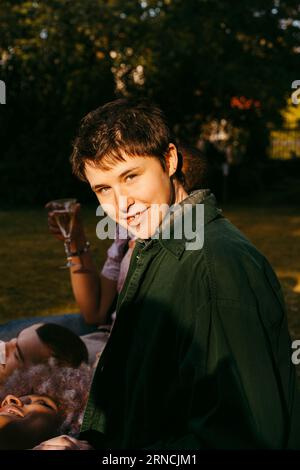 Ritratto laterale di una persona non binaria sorridente con gli amici nel cortile sul retro durante la giornata di sole Foto Stock