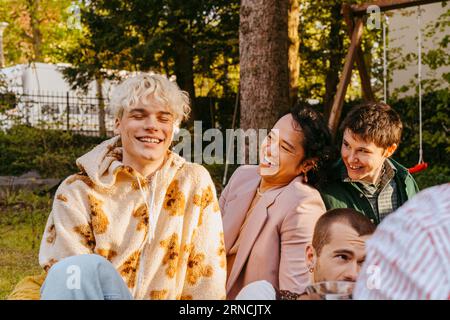Amici gay che ridono seduti l'uno accanto all'altro durante la cena in cortile Foto Stock