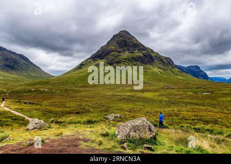 Un escursionista su un sentiero di fronte a una montagna sotto un cielo grigio e tempestoso Foto Stock