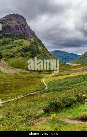 Hiking trail leading into a valley surrounded by steep mountains and a stormy, grey sky Stock Photo