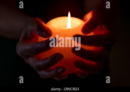 Female hands hold a round white candle with a burning flame Foto Stock