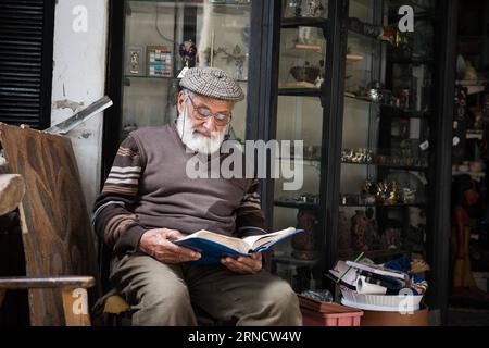 CAIRO, Mahamoud Sabry, un uomo d'affari di 81 anni, legge il Corano davanti al suo negozio di souvenir, il Cairo, Egitto, il 9 marzo 2016. Mahamoud Sabry continua a leggere ogni giorno. Oltre a finire di leggere l'intero Corano ogni 6 giorni, legge anche libri di poesia, storia e politica. Il 21° World Book and Copyright Day arriverà sabato. Un libro è un legame tra il passato e il futuro. È un ponte tra generazioni e culture diverse. E' una forza per creare e condividere saggezza e conoscenza. Ha detto il direttore generale dell'UNESCO Irina Bokova. Dopo cinque anni dall'epidemia di Th Foto Stock