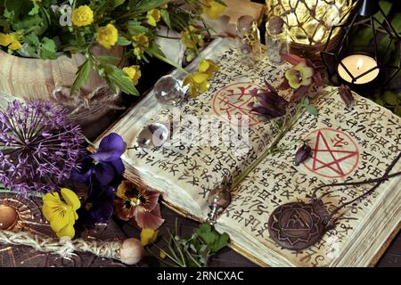 Natura morta con un libro magico aperto di incantesimi, candela e medaglione su un tavolo rituale delle streghe. Concetto occulto, esoterico e stregoneria. Sfondo mistico con Foto Stock