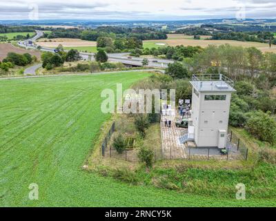 01 settembre 2023, Sassonia, Heinersgrün: La torre di confine di Heinersgrün, recentemente ristrutturata, nella regione del Vogtland, una volta parte della striscia della morte sul confine interno-tedesco (vista aerea con drone). Il testimone in pietra del regime di frontiera della DDR servirà in futuro come filiale del Museo tedesco-tedesco Mödlareuth e sarà aperto ai visitatori per visite. La torre era entrata in funzione nel 1978 come cosiddetto posto di comando. È una delle ultime reliquie della sicurezza di frontiera della RDT tra Sassonia e Baviera. Foto: Jan Woitas/dpa Foto Stock