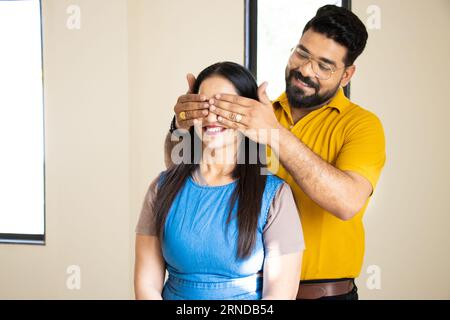 Un giovane indiano che chiude gli occhi della sua ragazza con la mano dandole una sorpresa. Foto Stock