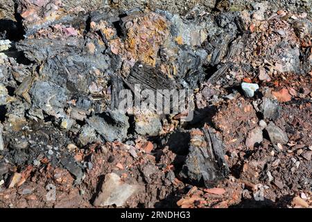 Strati di miniere di carbone colorate e rifiuti di altoforni insieme ad altri detriti industriali che vengono lentamente erosi e lavati via dal mare sul Foto Stock