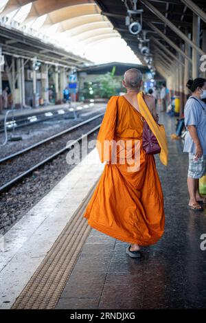 Scattata da dietro, questa foto mostra un monaco buddista in tradizionali vesti arancioni che camminano lentamente su una piattaforma tranquilla a Hua Lamphong. Foto Stock