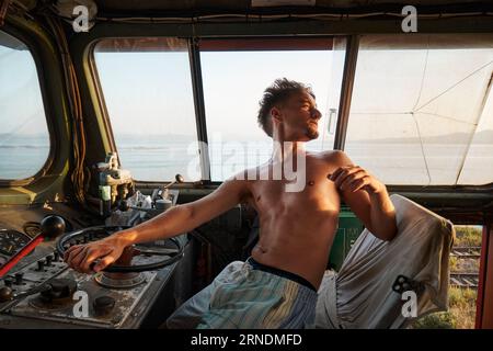 Un uomo caucasico seduto nella cabina di guida di una grande locomotiva che guarda indietro Foto Stock