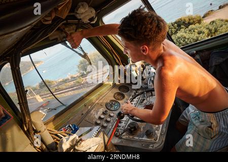 Un uomo caucasico nella cabina di guida di una grande locomotiva, che regola un componente sopra il finestrino Foto Stock