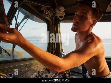 Un uomo caucasico nella cabina di guida di una grande locomotiva, che regola un componente sopra il finestrino Foto Stock