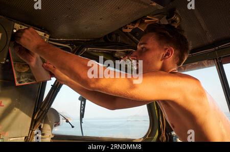 Un uomo caucasico nella cabina di guida di una grande locomotiva, che regola un componente sopra il finestrino Foto Stock