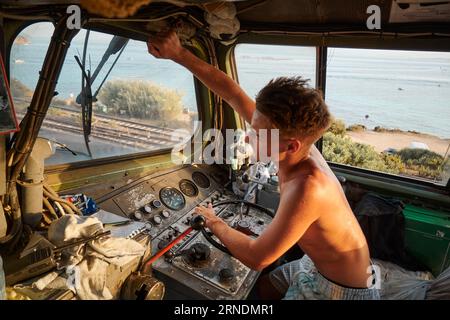 Un uomo caucasico nella cabina di guida di una grande locomotiva, che regola un componente sopra il finestrino Foto Stock