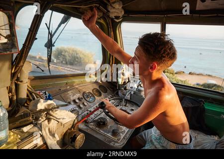 Un uomo caucasico nella cabina di guida di una grande locomotiva, che regola un componente sopra il finestrino Foto Stock