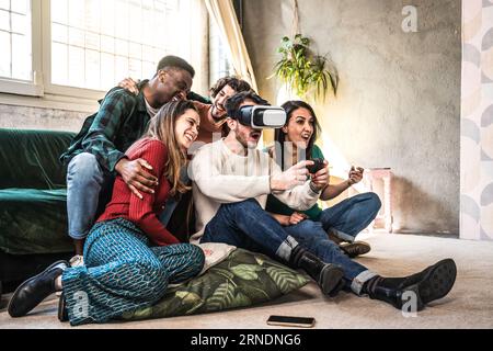 Felici amici multietnici seduti sul divano che giocano ai videogiochi con il visore VR 3d a casa: Allegro gruppo z di generazione che si diverte con il moderno technolo Foto Stock