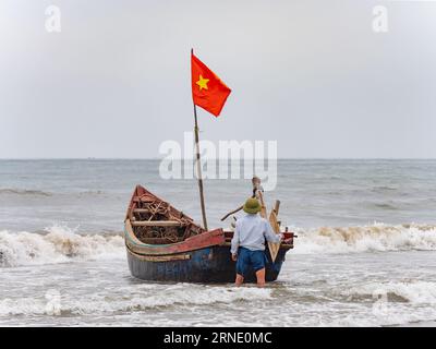 Fisherman lancia la sua barca contro il vento e le onde alte a Sam Son Beach, Thanh Hoa, Vietnam Foto Stock