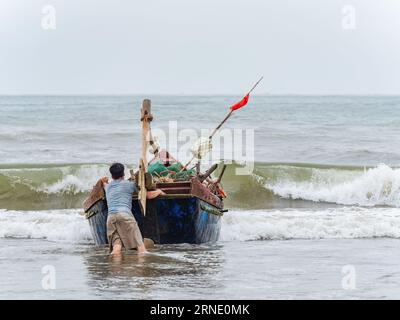 Fisherman lancia la sua barca contro il vento e le onde alte a Sam Son Beach, Thanh Hoa, Vietnam Foto Stock