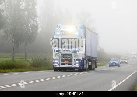 Scania Truck L Retva Oy personalizzato tira semirimorchio nel traffico stradale in una mattinata nebbiosa, con gli abbaglianti accesi brevemente. Salo, Finlandia. 25 agosto 2023. Foto Stock