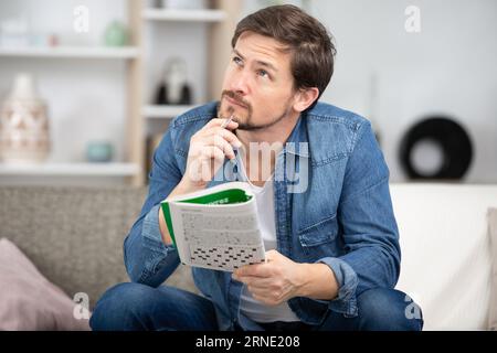 giovane uomo seduto facendo un puzzle crossword guardando pensieroso Foto Stock