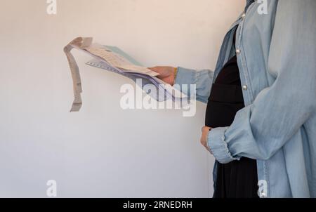 Donna incinta che detiene una ricevuta su sfondo bianco Foto Stock