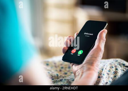 Old woman and phone call with hidden mobile number. Senior mature lady and fraud and scam caller. Love and romance hoax. Holding smartphone in hand. Stock Photo