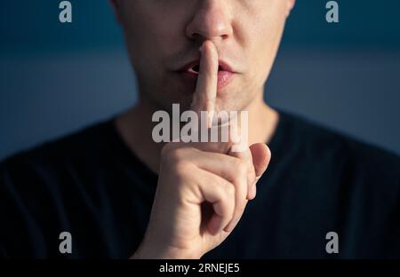Segreto e silenzio. Gesto shh silenzioso con il dito sulle labbra. Uomo che fa espressione con la mano sulla bocca. Argomento tabù, censura o libertà. Foto Stock