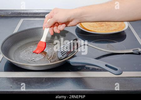 Mano umana maschile con una spazzola di silicio rosso mettere l'olio nella padella calda per cucinare dei pancake per colazione Foto Stock
