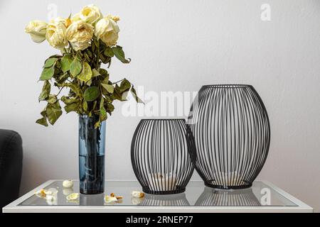 rose bianche invecchiate e asciugate nel tempo con foglie cadenti e fiori marcillati accanto alle candele in superficie il boquet di fiori simboleggia il cerchio organico di lif Foto Stock