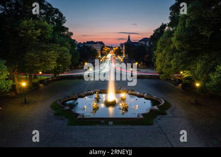 Fontana illuminata con getti d'acqua e sculture su una piazza di fronte al ponte Luitpold e Prinzregenten Street al crepuscolo a Monaco, Germania Foto Stock