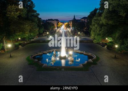 Fontana illuminata con getti d'acqua di fronte al ponte Luitpold e Prinzregenten Street all'ora blu al tramonto a Monaco, Baviera, Germania Foto Stock