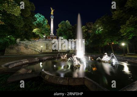 Fontana con getti d'acqua, sculture, scale e pilastro con l'angelo della pace nell'illuminazione notturna, Bogenhausen, Monaco, Germania Foto Stock